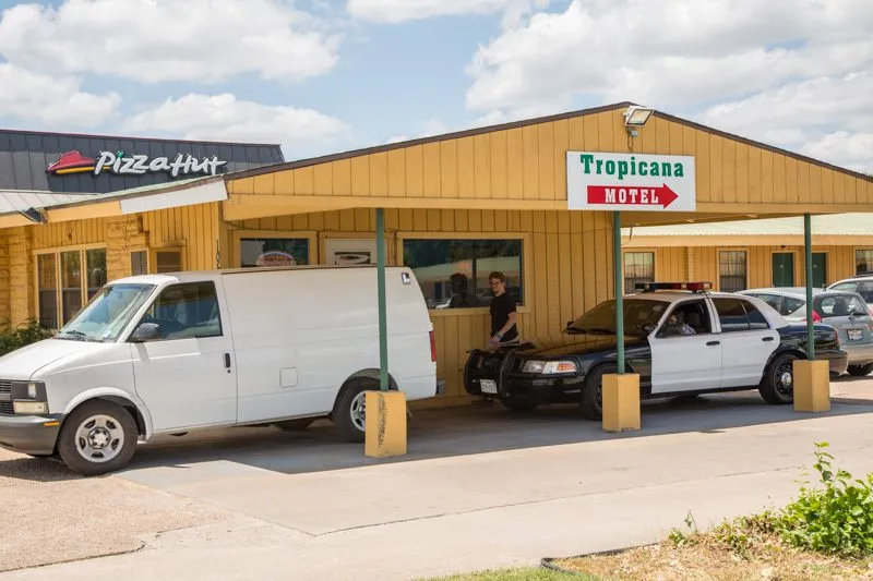 The white van and a police cruiser parked under the motel carport